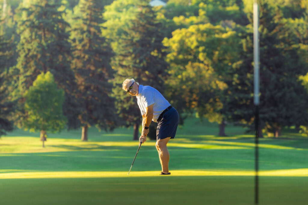 Stunning golfer putting on the lush greens at Highlands Golf Club, surrounded by beautiful trees.