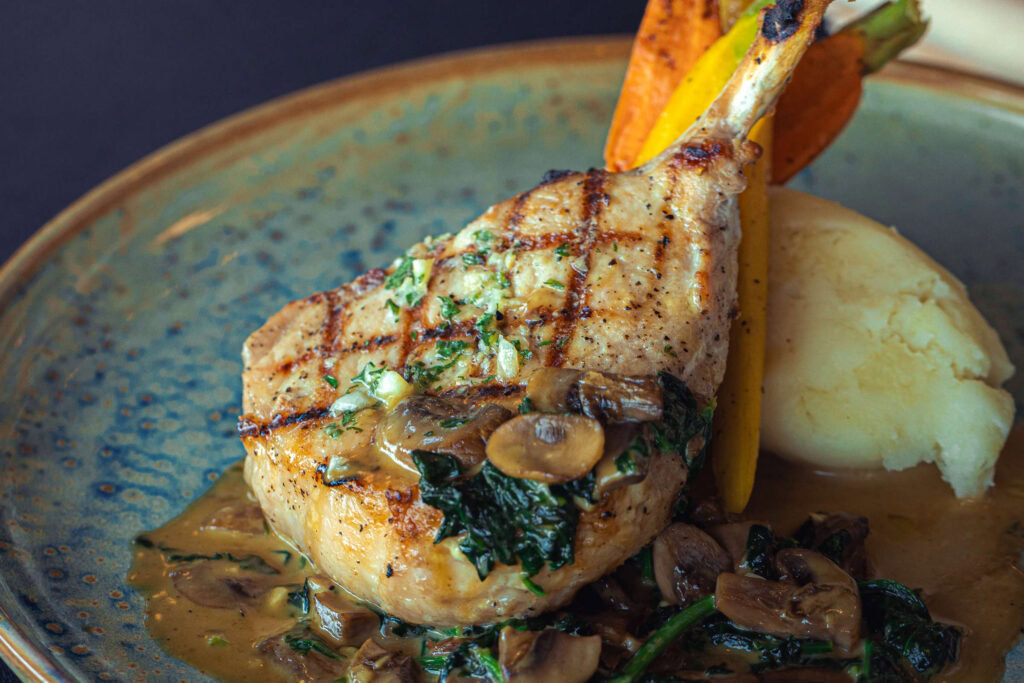 Succulent grilled lamb chop with mushroom sauce, mashed potatoes, and roasted vegetables.