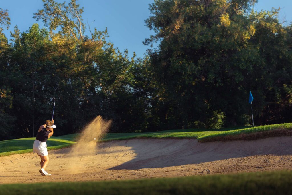 Sunset golf at Highlands Golf Club with sand dunes and lush trees in the background.