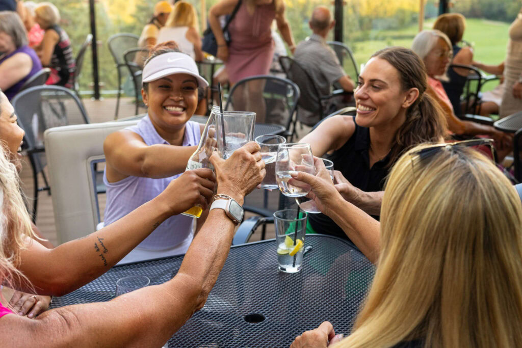 Cheerful women toasting drinks at Highlands Golf Club's outdoor patio.