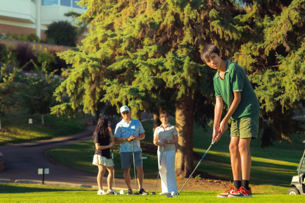 Young boy playing golf at Highlands Golf Club in scenic outdoor setting.