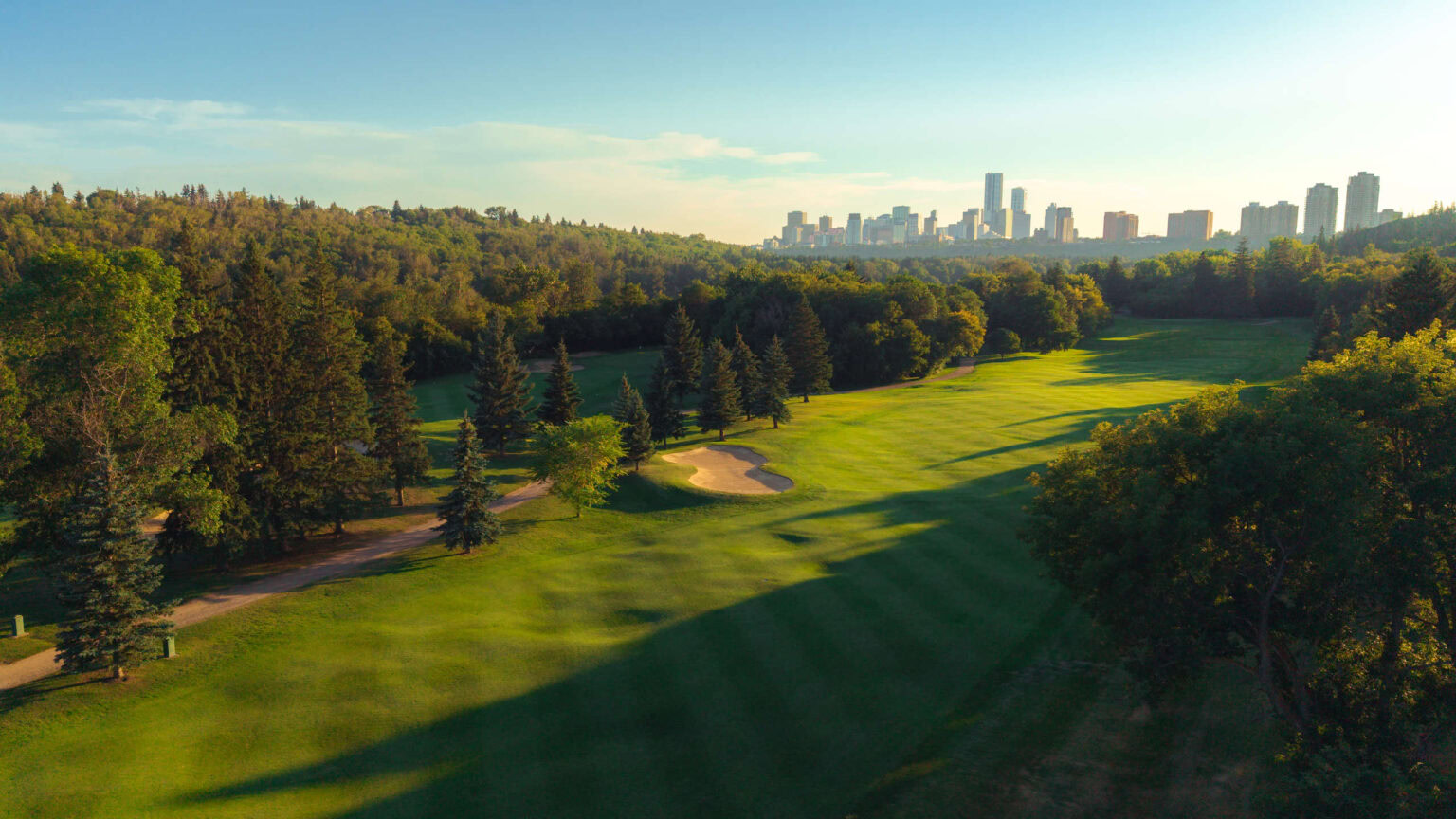 Lush green Highlands Golf Club with city skyline in the background.