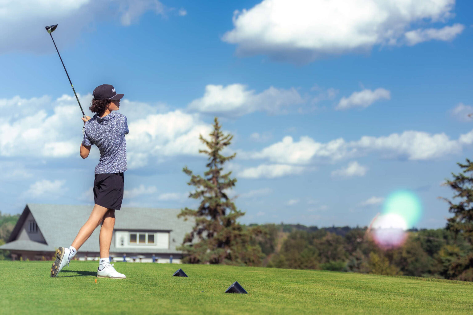 Vibrant golf course with a young female golfer teeing off under a blue sky.